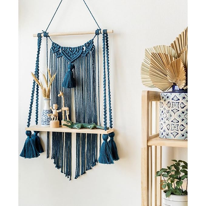 Blue macrame wall hanging shelf with wooden plank for books, plants, and home décor